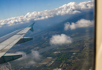 Fototapeta premium Landing in city of Vancouver. mountains, lakes and rivers outside a plane window. Travel time, sky, clouds and plane wing. Aerial view