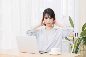 部屋でノートパソコンを使いながら耳を塞ぐ若い女性
