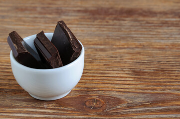 White porcelain bowl with dark chocolate pieces on wooden background. Copy space
