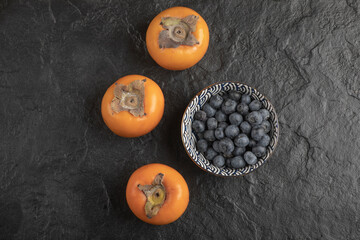 Ceramic bowl of delicious blueberries and persimmons on black surface