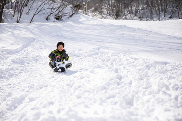 Fototapeta na wymiar 男の子がそりに乗って楽しんで遊んでいる　winter