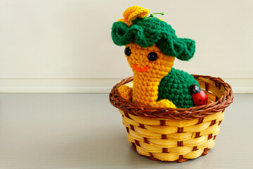 Knitted turtle sits in a wicker basket on a light background.