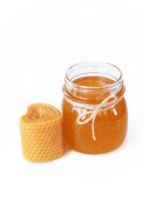 A jar of honey near a heart-shaped colored decorative natural beewax candle isolated on a white background. A delicate color palette. Close up	