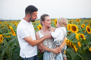 Happy family, mother father and kid together, hugging  and walking in the nature sunflowers field...