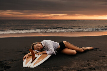 Beautifull woman on tropical beach holding surfboard at sunset in Bali