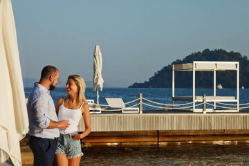 Loving couple enjoying honeymoon on territory beach hotel with luxury view walking shows emotion on sea background. Happy lovers on romantic trip fun on summer vacation. Concept romance and relaxation