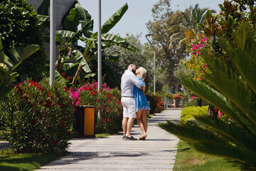 Fototapeta na wymiar Loving couple enjoying honeymoon in luxury hotel, walking through grounds with palm trees and beauty flowers. Happy lovers on romantic trip have fun on summer vacation. Concept romance and relaxation