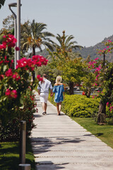 Fototapeta na wymiar Loving couple enjoying honeymoon in luxury hotel, walking through grounds with palm trees and beauty flowers. Happy lovers on romantic trip have fun on summer vacation. Concept romance and relaxation