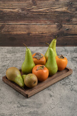 Delicious fuyu persimmons and ripe pears on wooden plate
