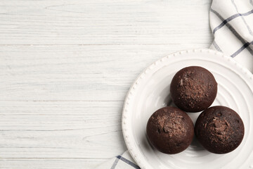 Delicious chocolate muffins on white wooden table, top view. Space for text