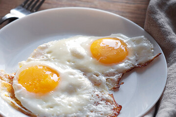 Scrambled eggs in a white plate on the table. A linen towel and a fork are nearby.
