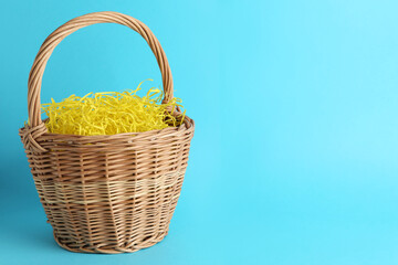 Fototapeta na wymiar Easter basket with yellow paper filler on light blue background, space for text