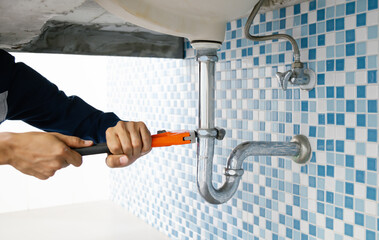 Plumber working in the bathroom, plumbing repair service, repairing leaking sinks with adjustable...