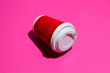 Red paper cup for coffee or tea to go on a pink background. Disposable tableware on a colored background with copy space.