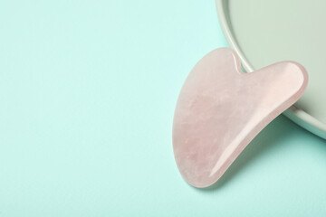 Rose quartz gua sha tool on turquoise background, space for text