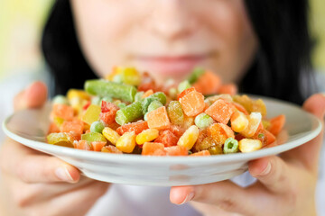 The girl is holding a plate of frozen vegetable mixture. The concept of diet and proper nutrition....