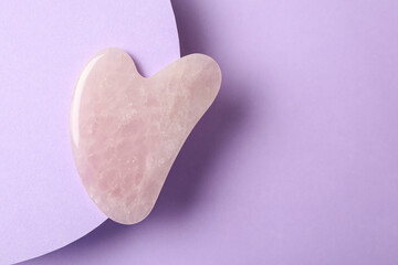 Fototapeta premium Rose quartz gua sha tool on violet background, top view. Space for text