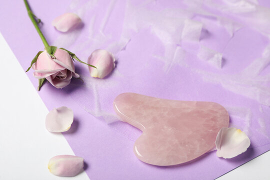 Rose quartz gua sha tool, facial mask and flower on white table