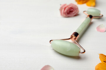 Natural jade face roller and flowers on white wooden background. Space for text