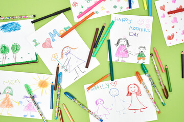 For the best mom. Top view of colorful child drawings for mothers day and felt tip pens lying on green table