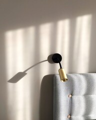 Minimalism and simplicity in bedroom decor. Beautiful light shining on wall with gold sconce and gray bed headrest. Scandinavian style.