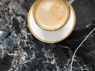 Beautiful cup of coffee with gold stripe on saucer and black marble table. Luxury tableware. Top view. Copy space. 