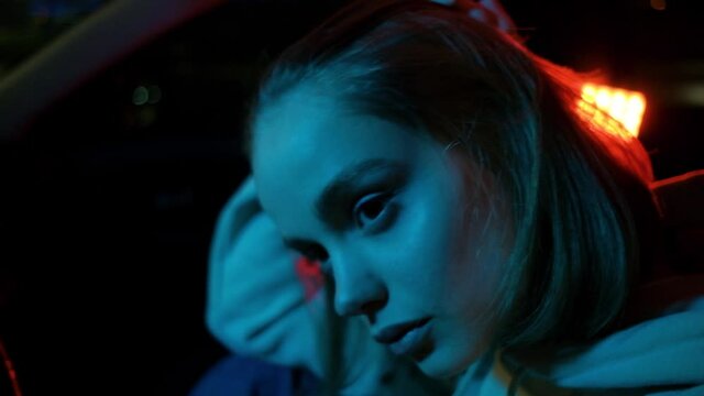 Portrait of a sad girl in a car in the evening city. Colored neon light.