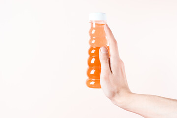 Fingers hold a jar of baby toy slime. Orange honey on a beige background