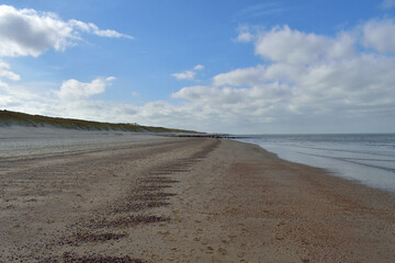 A wide open expanse of North Sea coastline and sandy beach at Domburg in the Netherlands under a blue cloudy sky.
