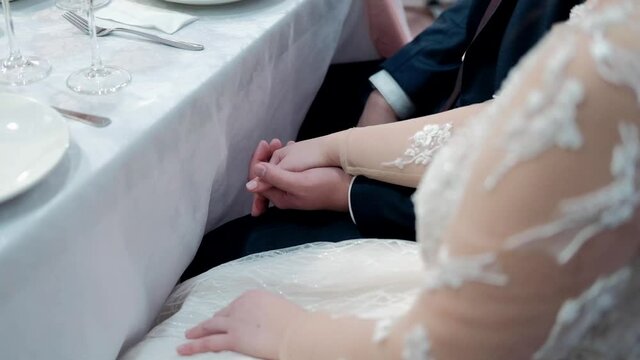 the groom holds the bride's hand while sitting at the table