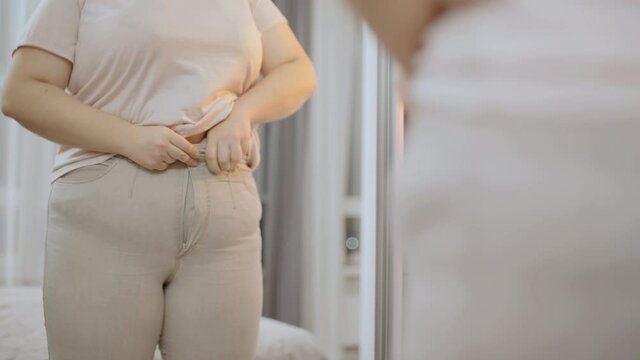 Oversize woman zipping up trousers, excess belly fat, unhealthy lifestyle, diet