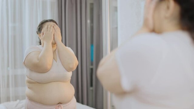 Desperate chubby woman with excess belly fat looking at mirror, insecurities