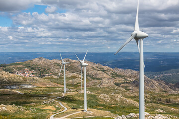 View of a top mountains landscape with a wind turbines, green herb fields and dirty road