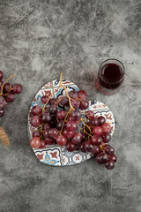 Cluster of red fresh grapes and glass of juice on marble table