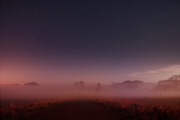 Obraz na płótnie Canvas Early morning foggy meadow with colorful moody color tones and night sky with stars