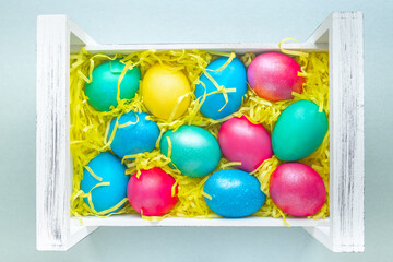 Colorful Easter eggs in a white wooden box on a light background. Selective focus. Close-up. Top view.