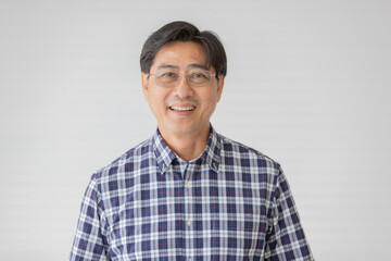 Portrait close up shot of middle aged asian male model with short black hair wearing blue plaid shirt with stand smiling in front of white background - Powered by Adobe