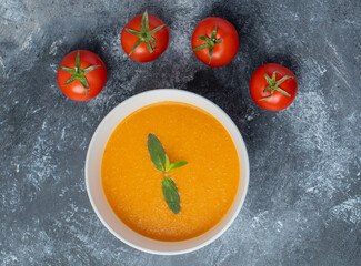 Tomato soup in white ceramic bowl with fresh tomatoes on grey background