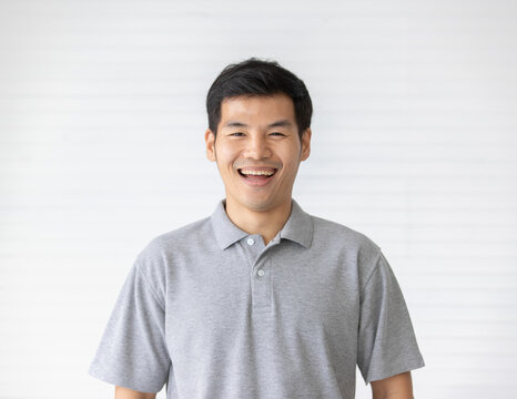 Portrait Close Up Shot Of Handsome Asian Male Model With Short Black Hair Wearing Gray Polo Shirt Stand Smiling In Front Of White Background