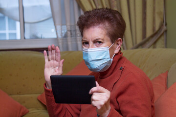 Senior woman wearing protective face mask talks with his family on video call during the...