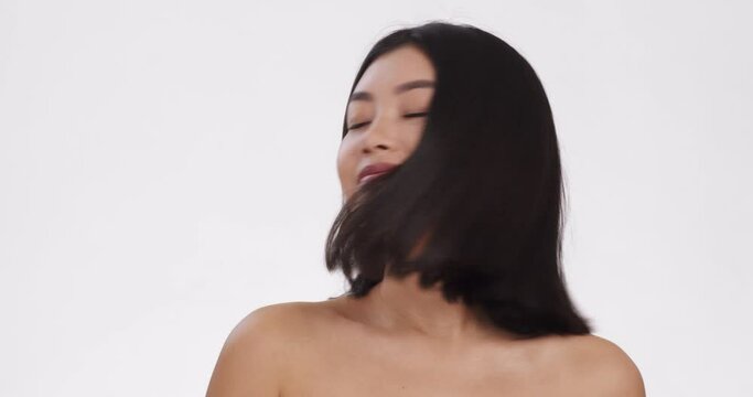 Perfect haircare. Portrait of young asian woman playing with her silky hair, white background, slow motion