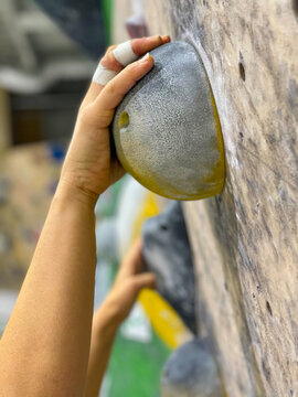 VERTICAL, CLOSE UP: Unrecognizable female climber hangs off yellow sloper holds.