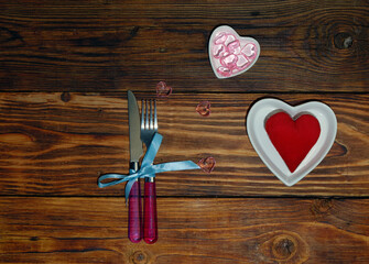 cutlery plate in the form of a heart on a wooden background background with a plush heart in it, glass hearts in a small plate and table