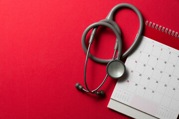 Top view of stethoscope and calendar on the red background, schedule to check up healthy concept