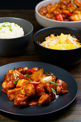Sweet and sour chicken, fried rice with egg and glass noodles salad served in ceramic bowls. Dark wooden table, high resolution