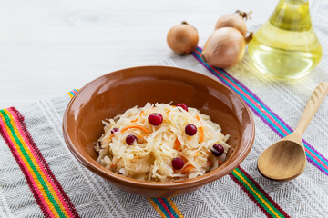 Sauerkraut with cranberries in a clay bowl with a wooden spoon on a towel. Russian traditional food. 