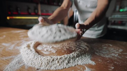 Close up of strong male hands making round form of dough on floured table. Professional pizzaiolo kneading base for pizza at restaurant. Cooking process.