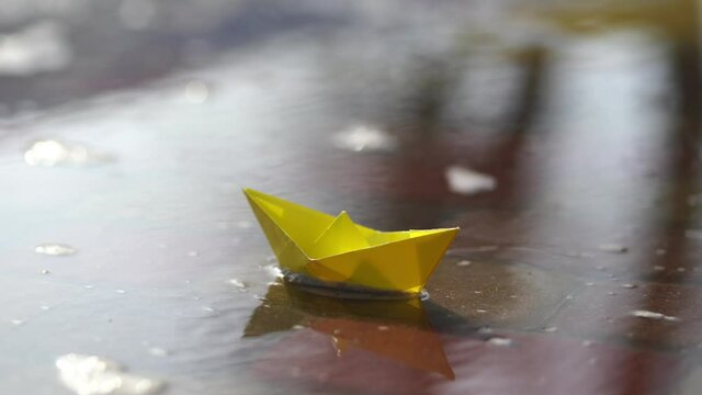 Melting snow and start of spring season concept. Big and huge puddles in snowy city park. Cute small yellow papper boat sailing in cold icy water on sidewalk outdoors