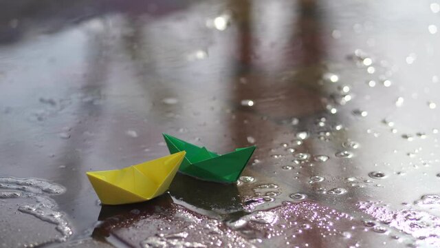 Melting snow and start of spring season concept. Big and huge puddles in snowy city park. Two cute small green and yellow papper boats swimming in water on sidewalk together