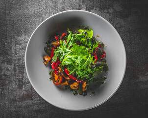 Vegetarian vegetable salad with mushrooms, arugula, tomato, beans and pepper in a bowl on Dark grey black slate background